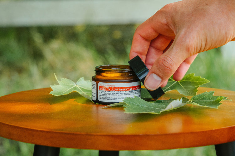 Hand lifting the lid from a jar of Ancient Nature bison tallow hydrating cream in natural light