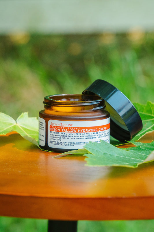 Open jar of bison tallow hydrating cream on wooden table with green leaves - natural face moisturizer by Ancient Nature